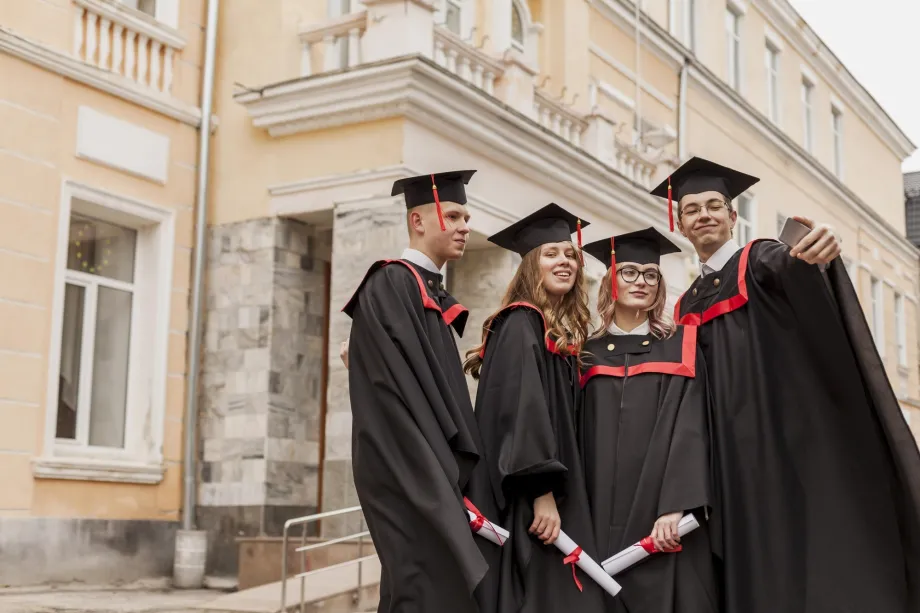 Skupina studenata u svečanim togama s diplomama u rukama snimaju selfie