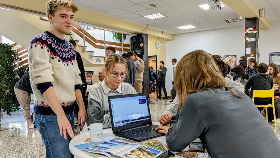 Skupina učenika sjedi za stolom i jedna učenica radi na laptopu