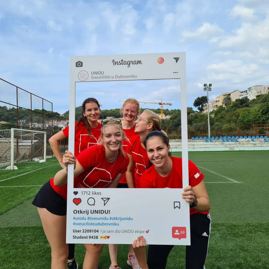 Pet djevojaka stoji na nogometnom igralištu. Dvije u rukama drže kartonski Instagram okvir i sve zajedno poziraju unutar tog okvira