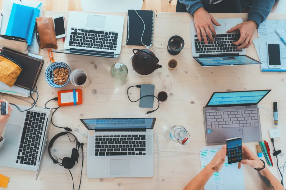Stol na kojem se nalazi pet laptopa, slušalice, šalice s kavom, mobiteli