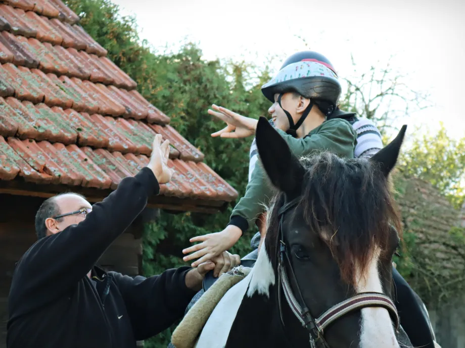 dječak sjedi na konju u pratnji odrasle osobe