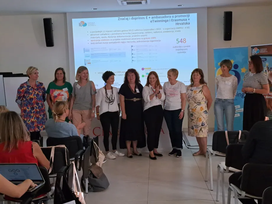 Ambasadori programa Erasmus + stoje u liniji. Iza njih je projekcija sa naslovom "Značaj i doprinos E+ ambasadora u promociji e Twinninga i Erasmusa+ Hrvatska"