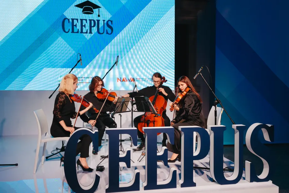 Četvero mladih osoba sviraju gudačke instrumente. Obučeni su u crno i sjede na pozornici. Ispred njih je veliki znak na kojem piše "CEEPUS" a iza njih je projektor na kojem piše "CEEPUS".