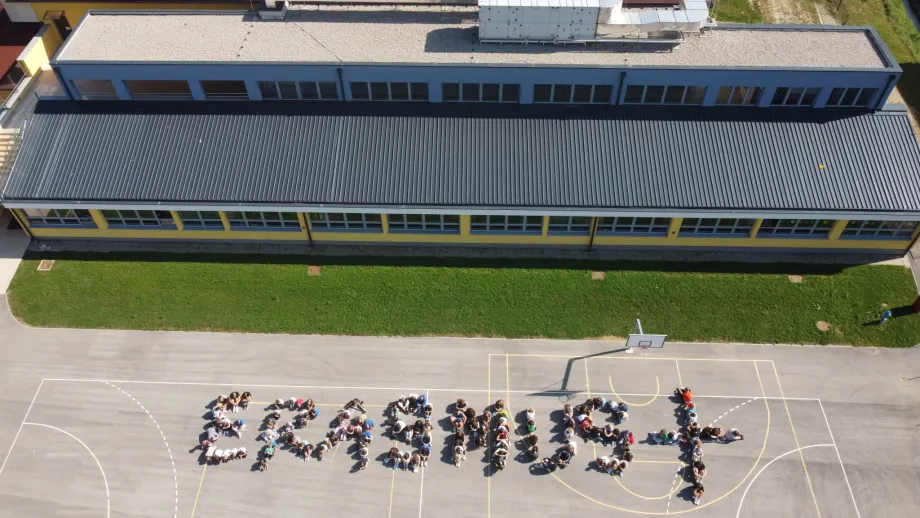 Slika iz ptičje perspektive na kojoj se vidi škola i igralište. Učenici stoje kako bi tvorili riječ "Erasmus+"