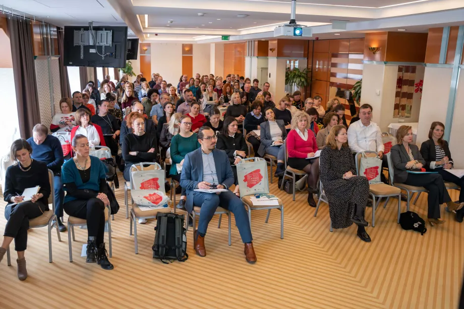 Stotinjak ljudi sjedi u kongresnoj dvorani i čeka početak programa.