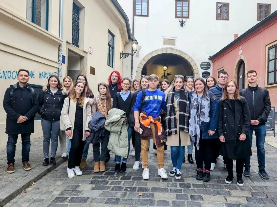 Dvadesetak mladih ljudi stoji ispred Kamenitih vrata u Zagrebu i pozira za fotografiju.