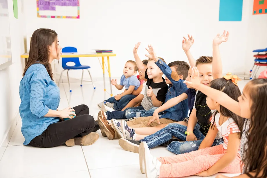 Pregled grupe učenika predškolske dobi koji podižu ruke pokušavajući sudjelovati u nastavi