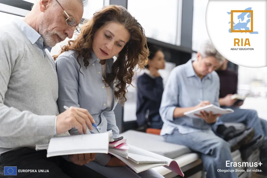 Srednjovječni muškarac drži otvoreni notes i razgovara sa ženom koja u rukama drži notes. U pozdaini se vide siluete još najmanje tri osobe