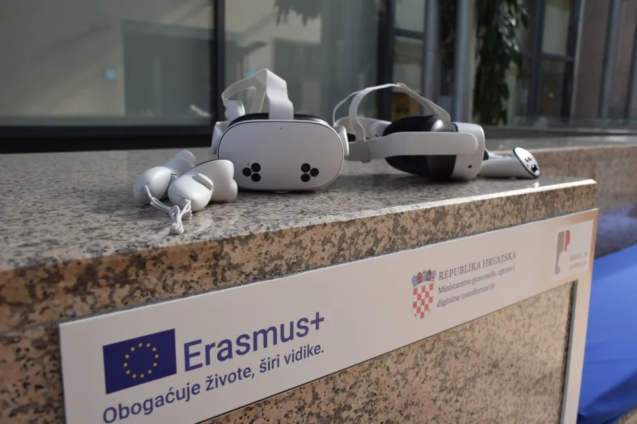 VR naočale na mramornoj podlozi pored okvira na kojem piše Erasmus+ i Ministarstvo pravosuđa, uprave i digitalne transformacije.
