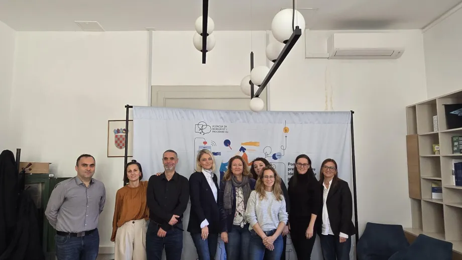 Devet muškaraca i žena na zajedničkoj fotografiji, u pozadini je platno s logotipom Agencije za mobilnost i programe EU-a i hrvatski grb na zidu