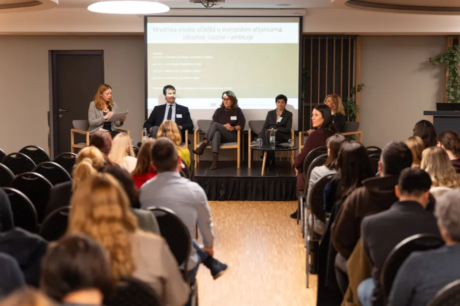 Panel rasprava, na pozornici se nalazi pet osoba u čijoj je pozadini projekcijsko platno, a ispred publika u dvorani