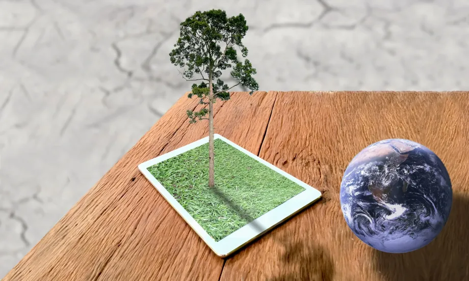 Na dvenom stolu su tablet s travnatim ekranom iz kojeg raste stablo i malena lopta kao zemaljska kugla