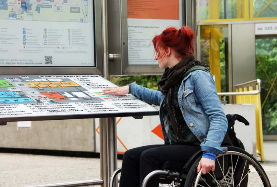 Žena u invalidskim kolicima čita sadržaj na ploči